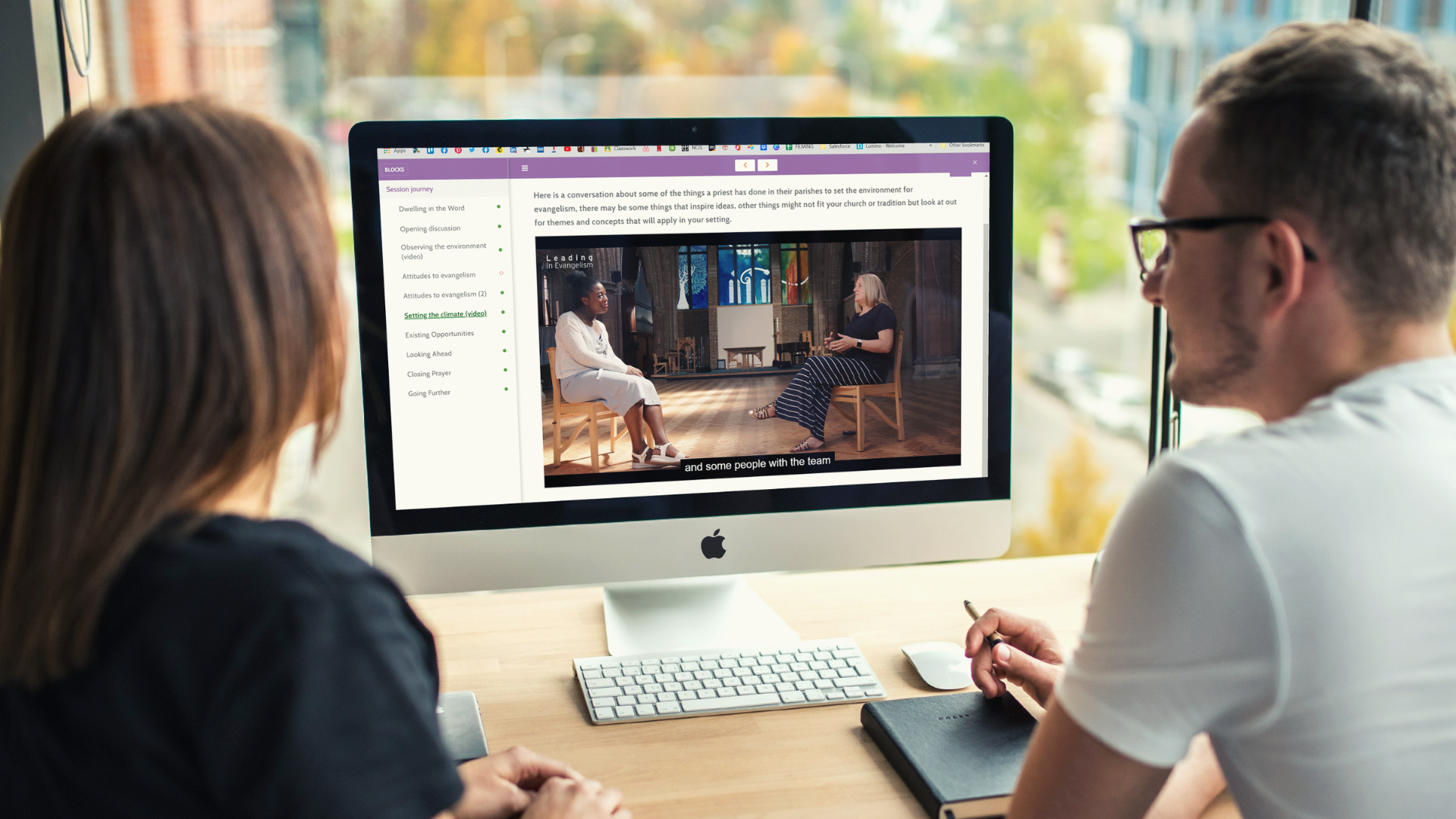 2 people sitting around a computer watching a video as part of the Leading in Evangelism resource